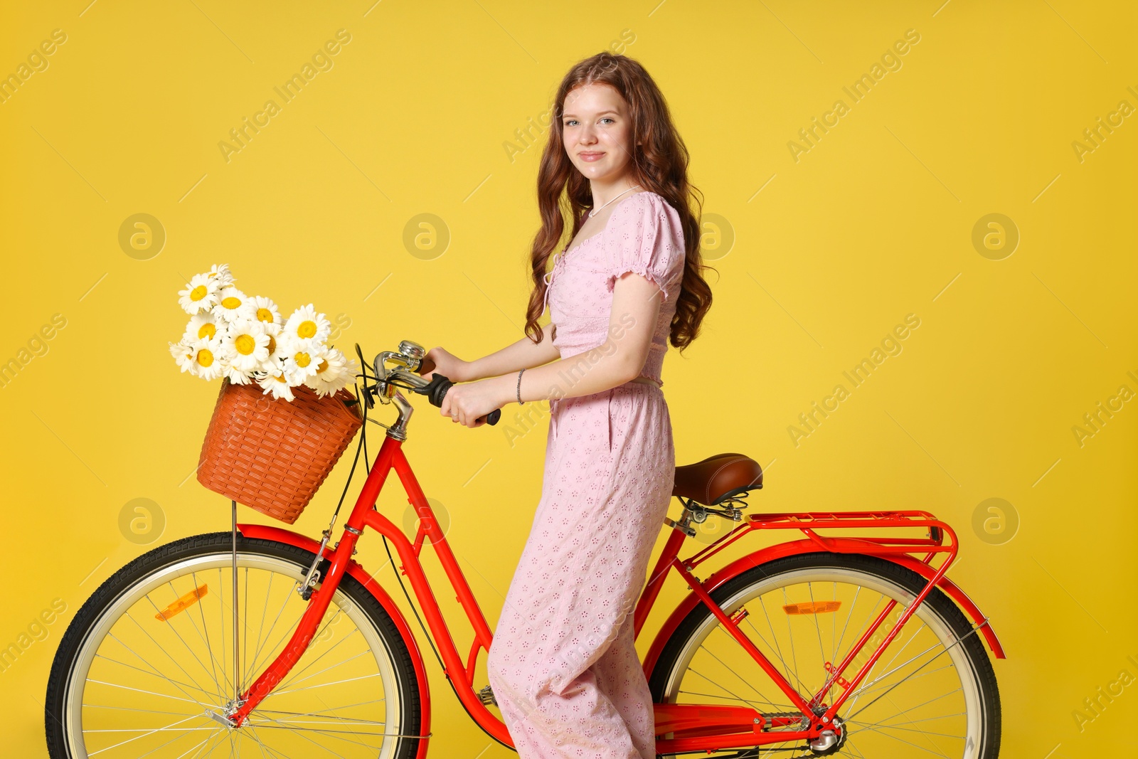 Beautiful teenage girl and bicycle with basket of flowers against yellow background Photo of Beautiful teenage girl and bicycle with basket of flowers against yellow background