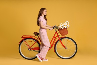 Photo of Smiling teenage girl and bicycle with basket of flowers against yellow background