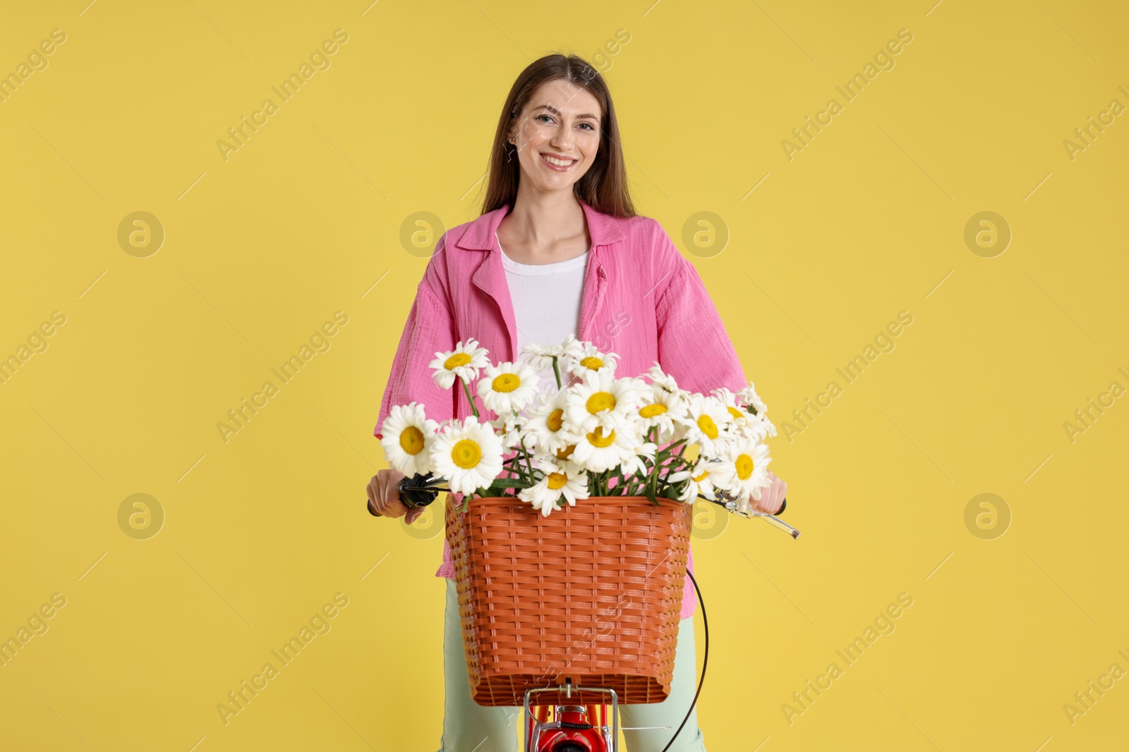 Smiling woman riding bicycle with basket of flowers against light green background Photo of Smiling woman riding bicycle with basket of flowers against light green background