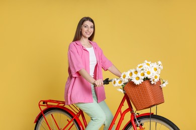 Photo of Smiling woman riding bicycle with basket of flowers against yellow background