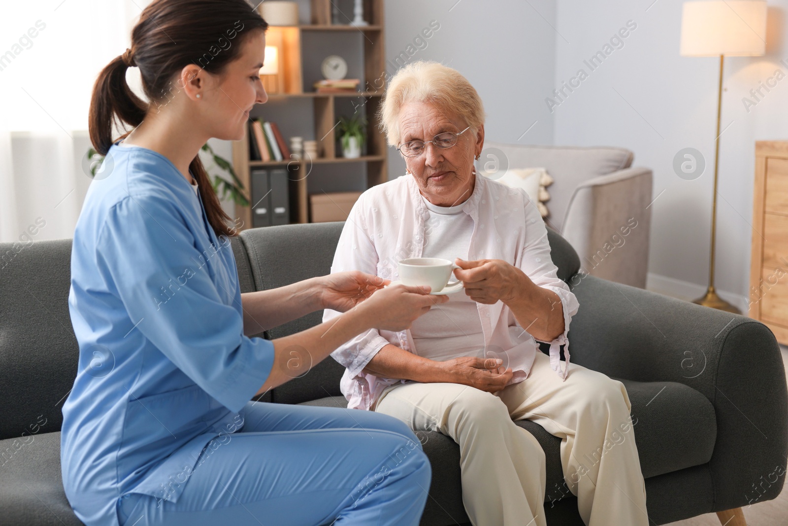 Photo of Nurse giving cup of drink to senior woman indoors. Home health care service