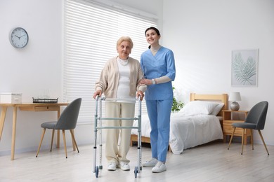 Photo of Nurse assisting senior woman with walking frame indoors. Home health care service