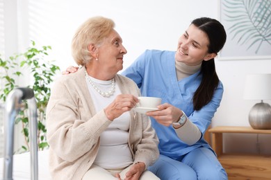 Photo of Nurse giving cup of drink to senior woman indoors. Home health care service