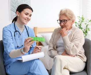 Photo of Nurse giving pills to senior woman indoors. Home health care service