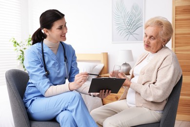 Photo of Nurse with clipboard examining senior woman indoors. Home health care service