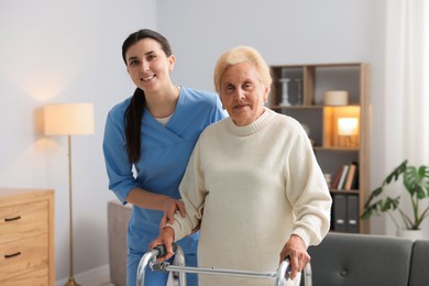 Photo of Nurse assisting senior woman with walking frame indoors. Home health care service