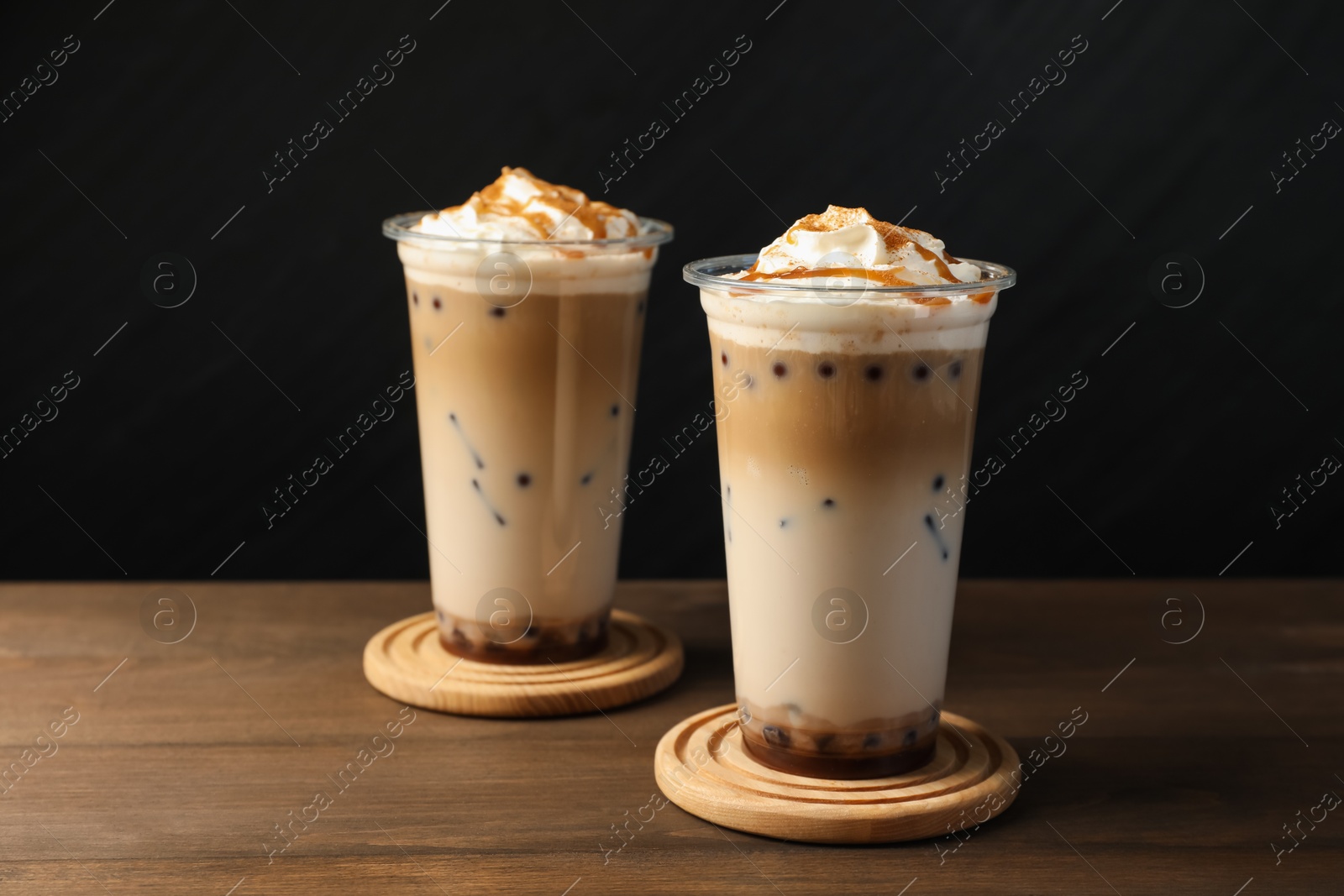 Tasty milk bubble tea in plastic cups on wooden table Photo of Tasty milk bubble tea in plastic cups on wooden table
