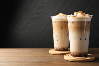 Photo of Tasty milk bubble tea in plastic cups on wooden table, closeup. Space for text