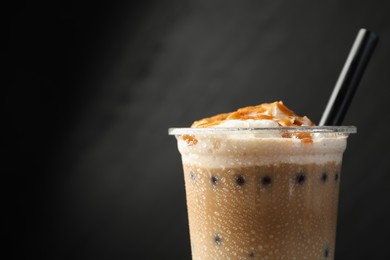 Photo of Tasty milk bubble tea in plastic cup on black background, closeup. Space for text