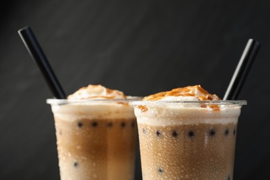 Photo of Tasty milk bubble tea in plastic cups on black background, closeup