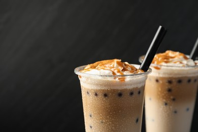 Photo of Tasty milk bubble tea in plastic cups on black background, closeup. Space for text