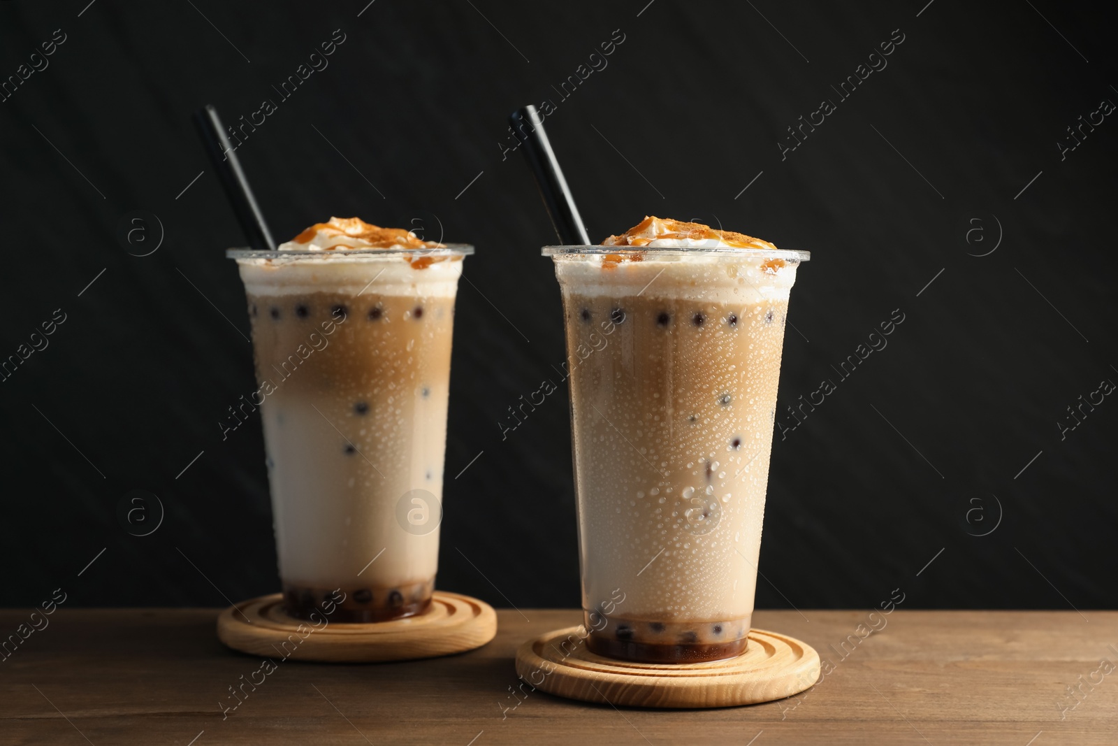 Tasty milk bubble tea in plastic cups on wooden table Photo of Tasty milk bubble tea in plastic cups on wooden table