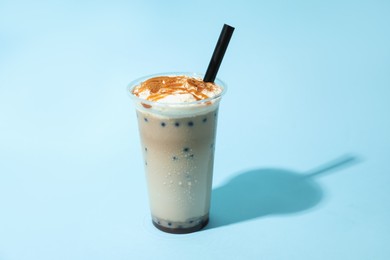 Photo of Tasty milk bubble tea in plastic cup on light blue background