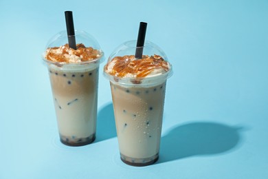 Photo of Tasty milk bubble tea in plastic cups on light blue background