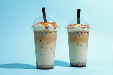 Photo of Tasty milk bubble tea in plastic cups on light blue background