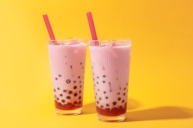 Photo of Tasty milk bubble tea in glasses on orange background