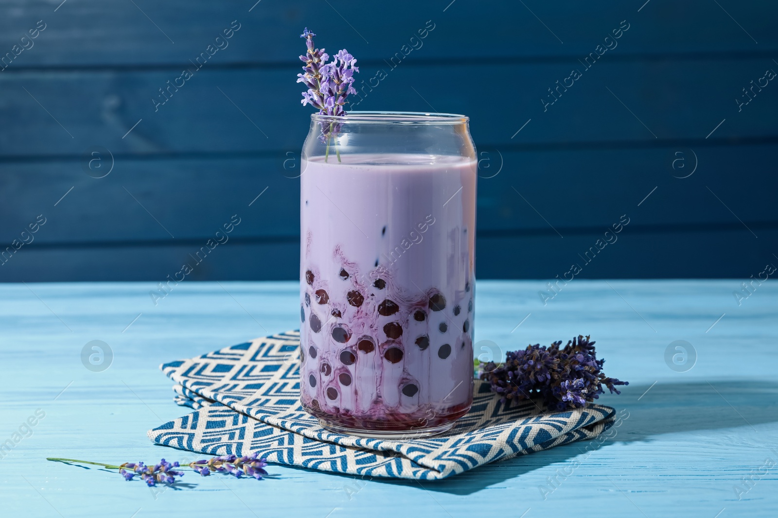 Tasty milk bubble tea in glass and lavender flowers on light blue wooden table, closeup Photo of Tasty milk bubble tea in glass and lavender flowers on light blue wooden table, closeup