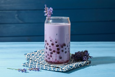Photo of Tasty milk bubble tea in glass and lavender flowers on light blue wooden table, closeup