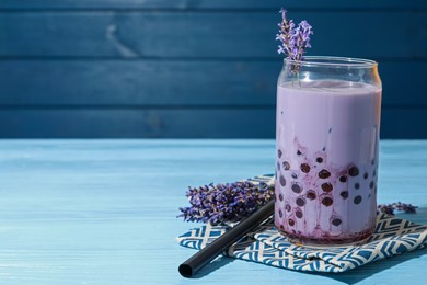 Photo of Tasty milk bubble tea in glass and lavender flowers on light blue wooden table, closeup. Space for text