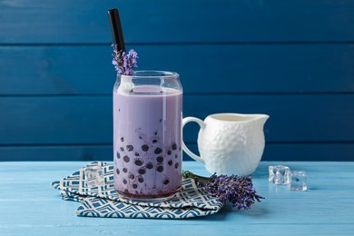 Photo of Tasty milk bubble tea in glass and lavender flowers on light blue wooden table