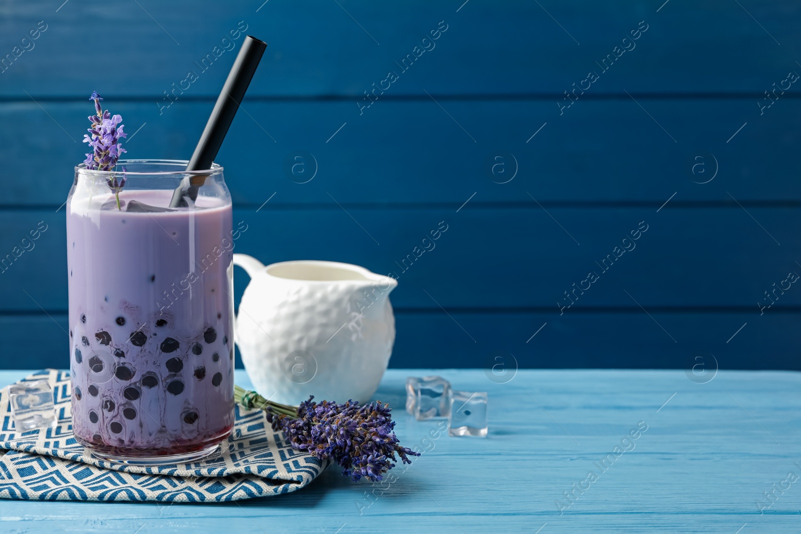 Tasty milk bubble tea in glass and lavender flowers on light blue wooden table, closeup. Space for text Photo of Tasty milk bubble tea in glass and lavender flowers on light blue wooden table, closeup. Space for text