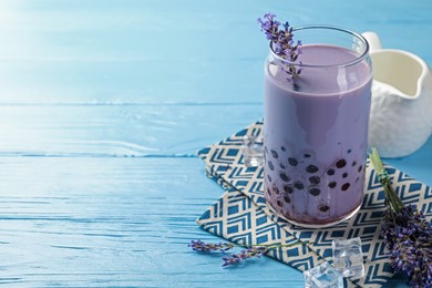 Photo of Tasty milk bubble tea in glass and lavender flowers on light blue wooden table, closeup. Space for text