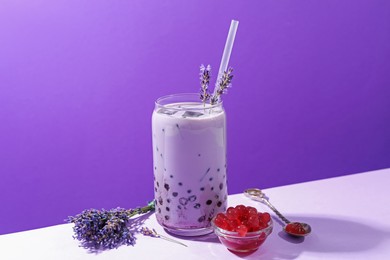 Photo of Tasty milk bubble tea in glass on white table against purple background