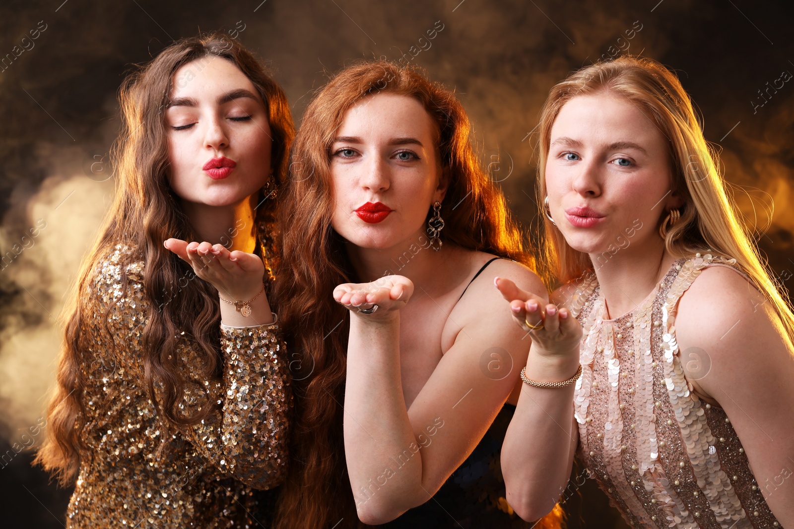 Beautiful women with different hair colors blowing kisses on dark background with smoke Photo of Beautiful women with different hair colors blowing kisses on dark background with smoke