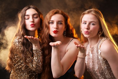 Photo of Beautiful women with different hair colors blowing kisses on dark background with smoke