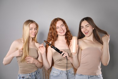 Photo of Beautiful women with different hair colors holding curling iron, shampoo and brush on grey background
