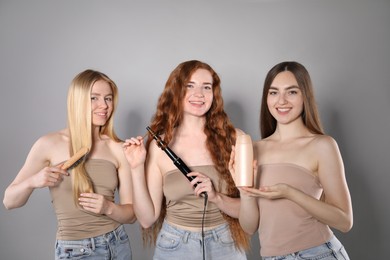 Photo of Beautiful women with different hair colors holding curling iron, shampoo and brush on grey background