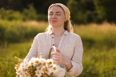 Photo of Happy woman with basket full of beautiful wildflowers outdoors