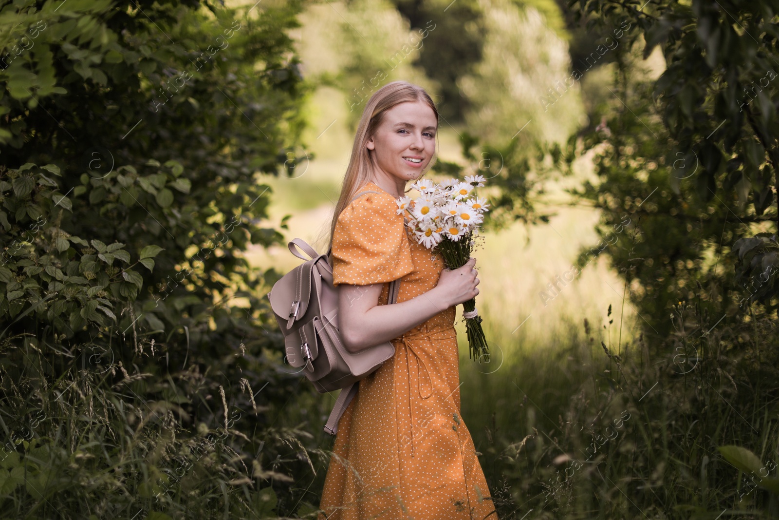 Beautiful woman with bouquet of wildflowers and backpack in forest Photo of Beautiful woman with bouquet of wildflowers and backpack in forest