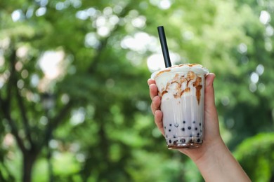 Photo of Woman with tasty milk bubble tea in plastic cup outdoors, closeup. Space for text