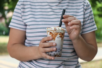 Photo of Woman with tasty milk bubble tea in plastic cup outdoors, closeup