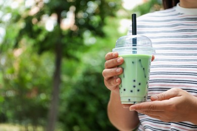 Photo of Woman with tasty milk bubble tea in plastic cup outdoors, closeup. Space for text