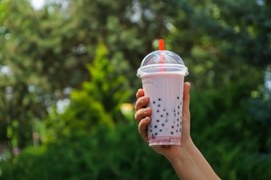 Photo of Woman with tasty milk bubble tea in plastic cup outdoors, closeup. Space for text