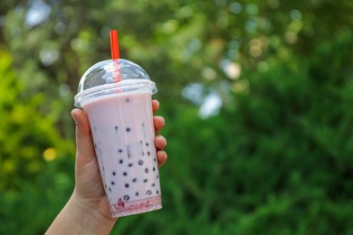 Photo of Woman with tasty milk bubble tea in plastic cup outdoors, closeup. Space for text