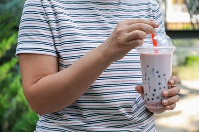Photo of Woman with tasty milk bubble tea in plastic cup outdoors, closeup