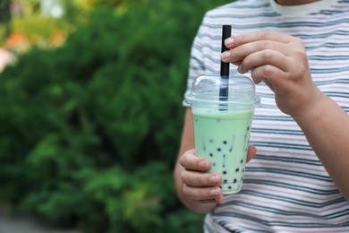 Photo of Woman with tasty milk bubble tea in plastic cup outdoors, closeup. Space for text