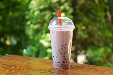 Photo of Tasty milk bubble tea in plastic cup on wooden table