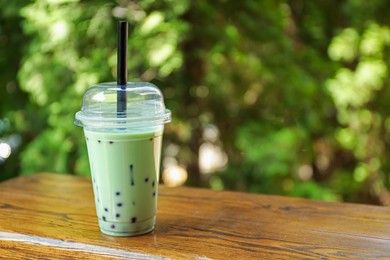 Photo of Tasty milk bubble tea in plastic cup on wooden table. Space for text