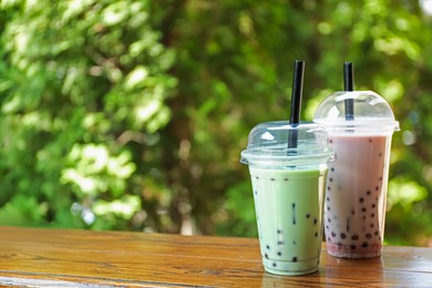 Photo of Tasty milk bubble tea in plastic cups on wooden table. Space for text