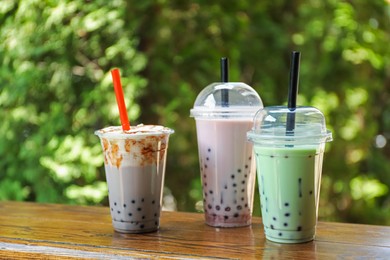 Photo of Tasty milk bubble tea in plastic cups on wooden table