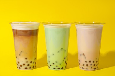 Photo of Tasty milk bubble tea in plastic cups on yellow background