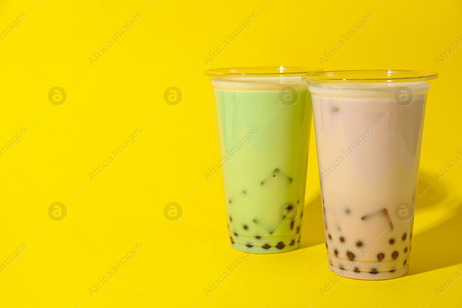 Tasty milk bubble tea in plastic cups on yellow background. Space for text Photo of Tasty milk bubble tea in plastic cups on yellow background. Space for text