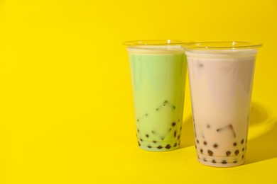 Photo of Tasty milk bubble tea in plastic cups on yellow background. Space for text