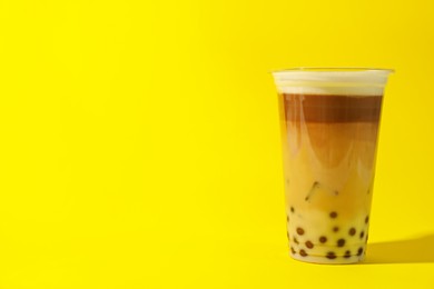 Photo of Tasty milk bubble tea in plastic cup on yellow background. Space for text