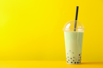 Photo of Tasty milk bubble tea in plastic cup on yellow background. Space for text
