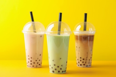Photo of Tasty milk bubble tea in plastic cups on yellow background
